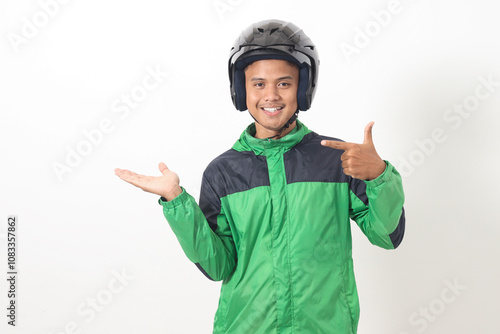 Portrait of Asian online taxi driver wearing green jacket and helmet pointing at empty space with finger. Isolated image on white background photo