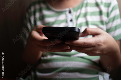 A person is holding a mobile phone with both hands and looking at the screen, wearing a green and white striped shirt. This suggests activities such as texting or browsing the internet on the phone.