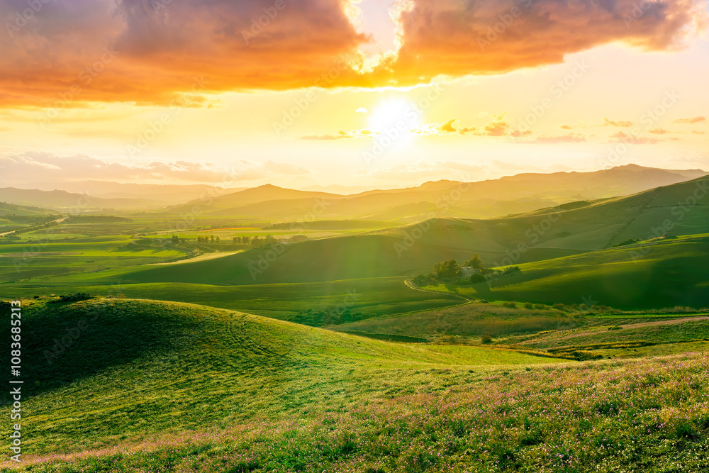 Obraz premium spring season green landscape of green field and meadow in a hill countryside with mountains and beautiful sunset sky on background