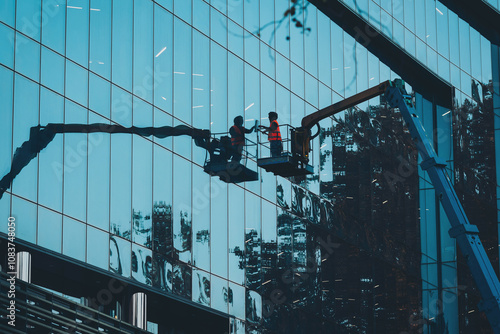 Male window cleaner cleaning glass windows on modern building high in the air on a lift platform. Worker glass high in the air. A worker washes windows in a building from a crane platform photo