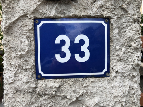 Shiny blue address plate that says number 33 on a stucco wall