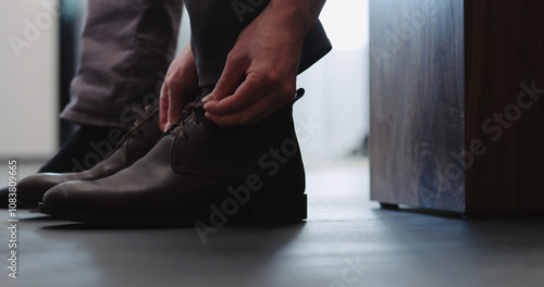 Young man put on his brown leather chukka boots indoor photo