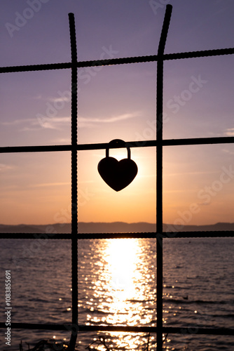 Heart-shaped love lock on fence at sunset with golden reflection on Lake Garda, Sirmione, Italy
