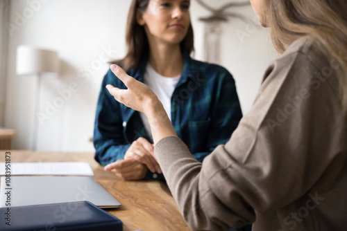 Cropped close up shot two women lead dialogue seated at workplace table, employee provide explanation to apprentice, share opinion, working together on joint task or project met in office. Interaction