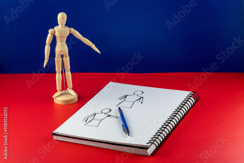 Artists Wooden Model with Sketch Pad and Pencil on a Red Base and Blue Background photo