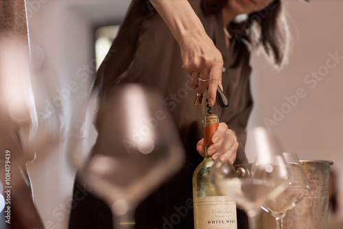 Medium close up of unrecognizable women opening wine bottle with metal corkscrew photo