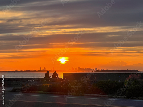 sunset over the city with a silhouette of a man and woman sitting on a stone wall
