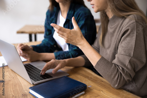 Close up, two women sit at table with laptop, lead conversation, discussing work-related topic, review business plan or project details, going over presentation slides or data. Teamwork, joint task photo