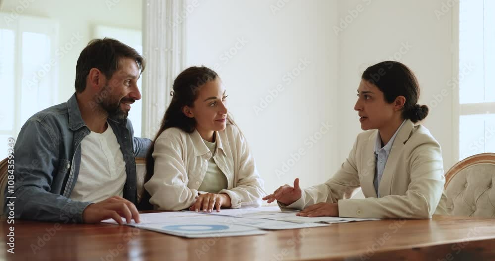 Happy Latin couple meeting with Indian financial advisor, consultant, discussing financial statistic data at table, talking, discussing insurance, investment, planning loan, mortgage, counting profit