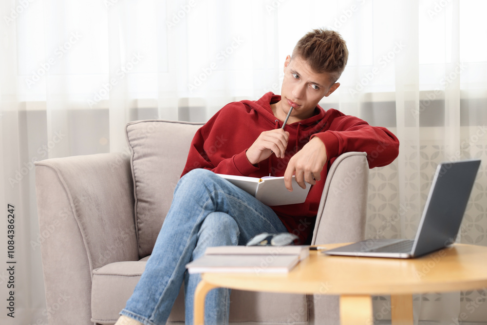 Student taking notes while studying in armchair at home Student taking notes while studying in armchair at home