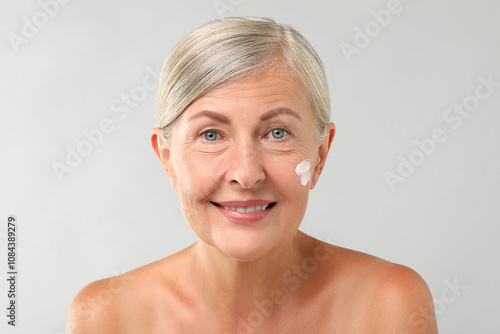 Senior woman with face cream on light background