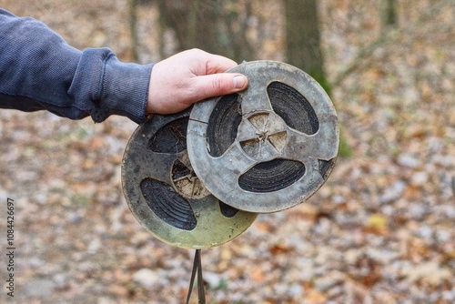 two old retro discarded plastic round music spools with magnetic dirty  brown tape reel in the hand of a man  on the street during the day
 photo