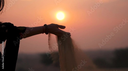 Sunset silhouette shot of desert sand falling from Indian woman's hand at Thar desert, Jaisalmer, Rajasthan, India. Sunset sky and desert sand. Travel and holidays concept.