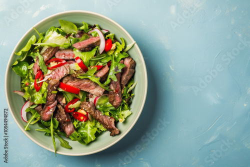 Top view of a bowel of Thai beef salad on light blue background with copy space