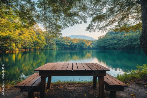Serene lakeside setting with wooden picnic table amidst lush greenery in earl...