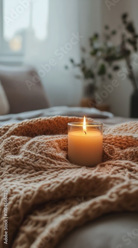Cozy bedroom setting with a lit candle on a soft blanket and a view of natura...