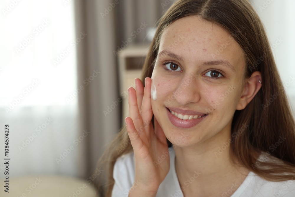 Teenage girl applying cream onto face at home, space for text. Acne treatment Teenage girl applying cream onto face at home, space for text. Acne treatment