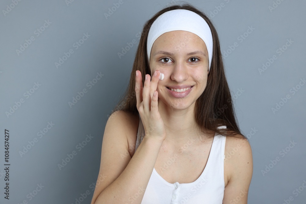 Teenage girl with acne problem applying cream on grey background Teenage girl with acne problem applying cream on grey background