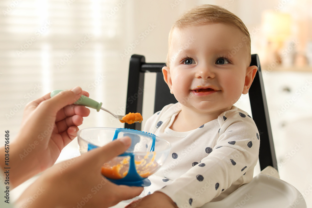 Mother feeding her cute little baby in high chair at home, closeup Mother feeding her cute little baby in high chair at home, closeup