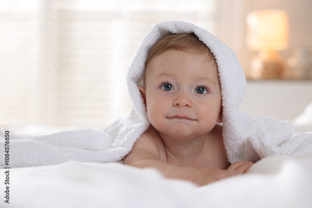 Cute baby under terry towel lying on bed at home Cute baby under terry towel lying on bed at home