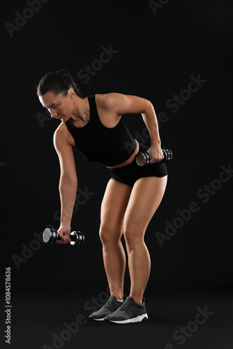 Woman exercising with dumbbells on black background