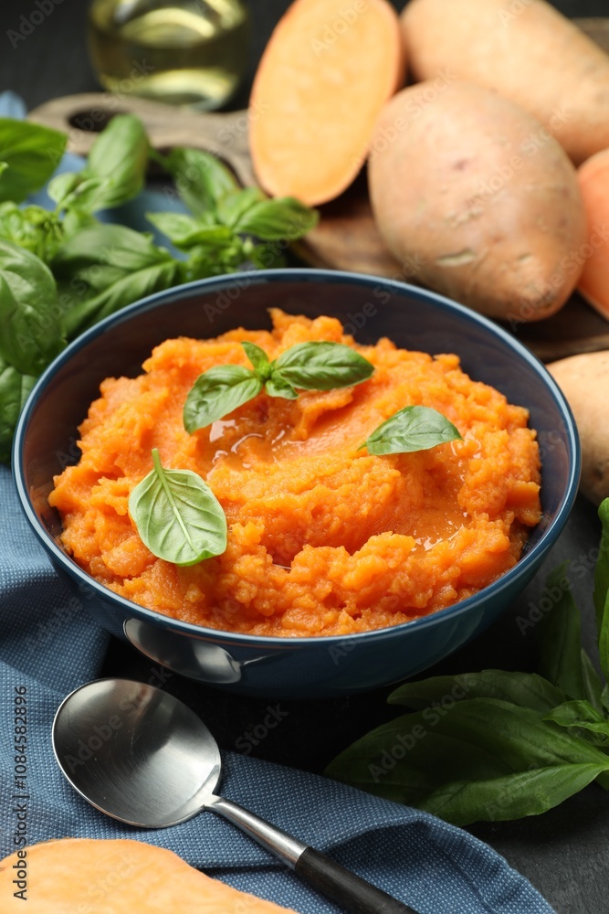 Tasty mashed sweet potato with basil in bowl, fresh vegetables and spoon on table, closeup Tasty mashed sweet potato with basil in bowl, fresh vegetables and spoon on table, closeup