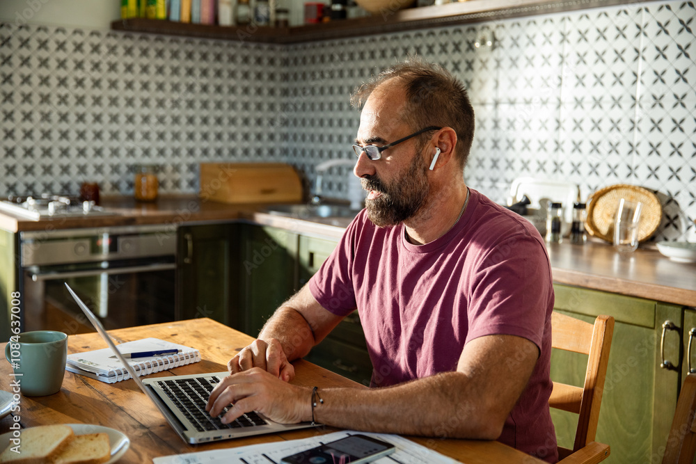 Man working on laptop at kitchen table Man working on laptop at kitchen table