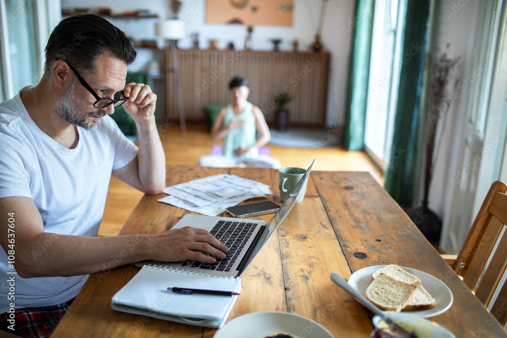 Woman doing morning yoga while man works on laptop at home Woman doing morning yoga while man works on laptop at home