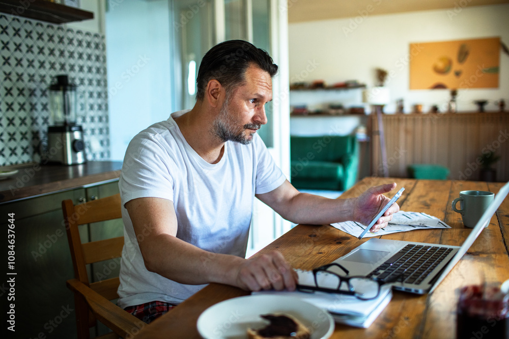 Man managing bills with laptop on kitchen desk Man managing bills with laptop on kitchen desk
