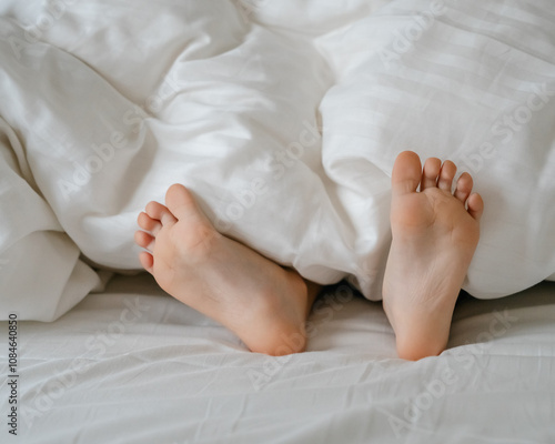 The feet of a small child in a parent's bed on white sheets rolled in a white blanket 