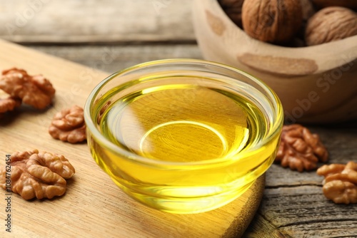 Cooking oil in bowl and walnuts on wooden table, closeup