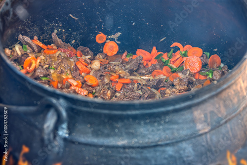 cooking traditional food stew in a three legged pot cauldron outdoors in the yard, african village life photo