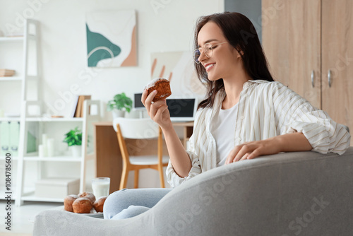 Young woman with tasty muffin sitting in armchair at home