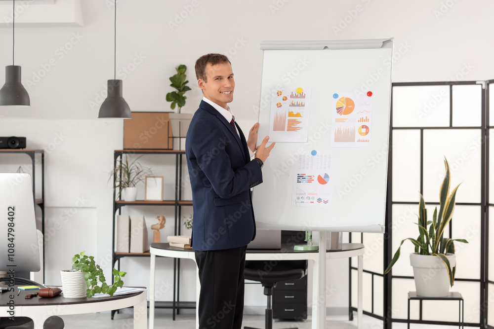 Handsome businessman working near diagrams on flipchart in office Handsome businessman working near diagrams on flipchart in office