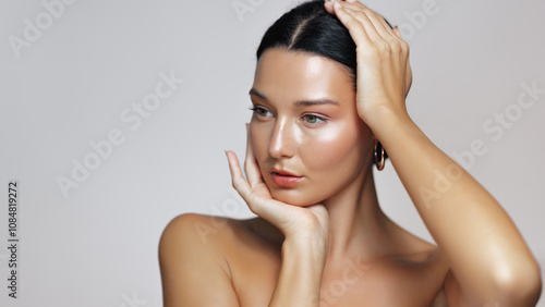 An elegant woman with sleek black hair and tanned, moisturized skin poses with hoop earrings in a beauty shot. Her glowing complexion, natural makeup, and bare shoulders enhance the sophisticated look