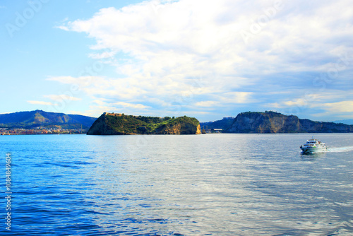 Picture-perfect view from the Gulf of Naples at the Tyrrhenian Sea and its unreal weavy scintillating mirror-like surface, a white boat on the right and rocky outcrops with greenery in the back photo