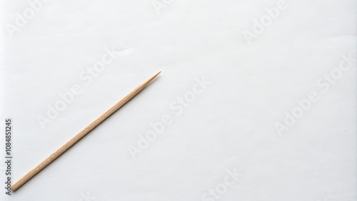 A single wooden toothpick rests on a plain white surface