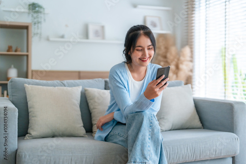 Wallpaper Mural Smiling pretty young Asian woman sitting on cozy couch, using funny mobile apps in living room. Woman at home, Doing online shopping, Messaging friends, Posting on social media Torontodigital.ca