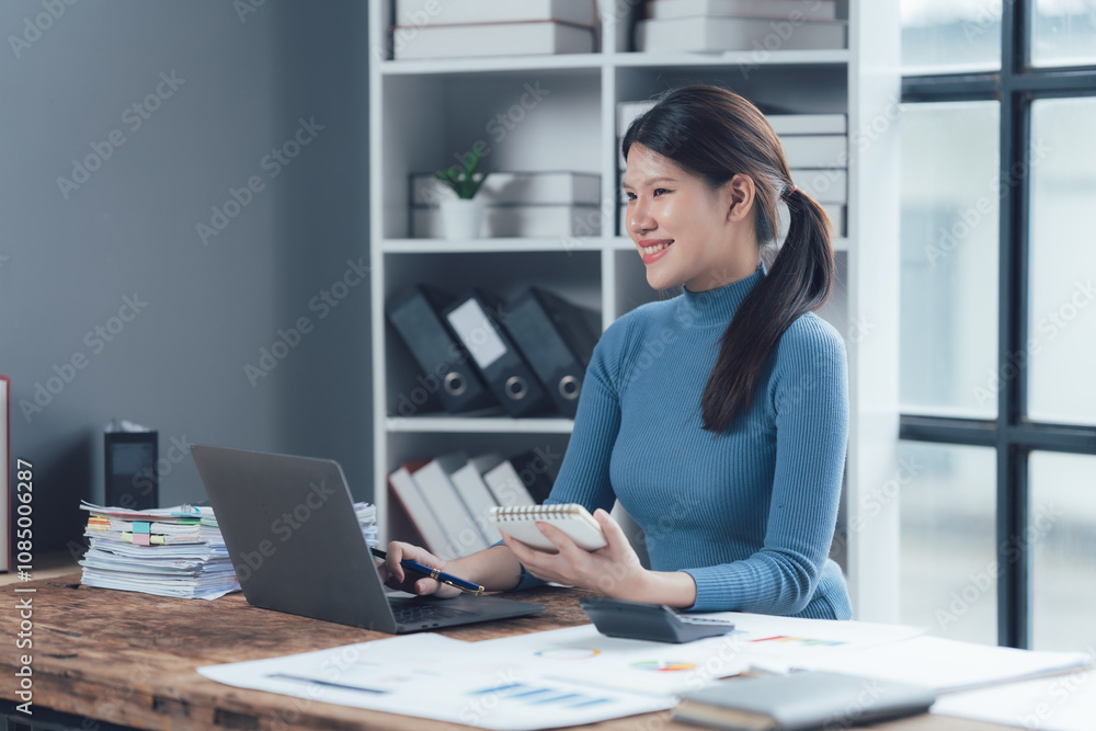 Smiling Businesswoman at Work: A young, Asian businesswoman smiles confidently as she works on her laptop and phone in her modern office. The image conveys professionalism, efficiency, and success. Smiling Businesswoman at Work: A young, Asian businesswoman smiles confidently as she works on her laptop and phone in her modern office. The image conveys professionalism, efficiency, and success.