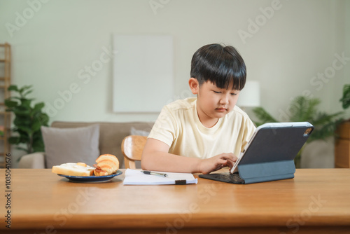 A mother teaches her son to study online at home, using a digital tablet for learning. They sit together at a table with snacks, promoting homeschooling and family bonding.