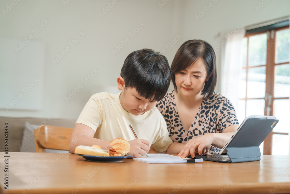 A mother teaches her son to study online at home, using a digital tablet for learning. They sit together at a table with snacks, promoting homeschooling and family bonding. A mother teaches her son to study online at home, using a digital tablet for learning. They sit together at a table with snacks, promoting homeschooling and family bonding.