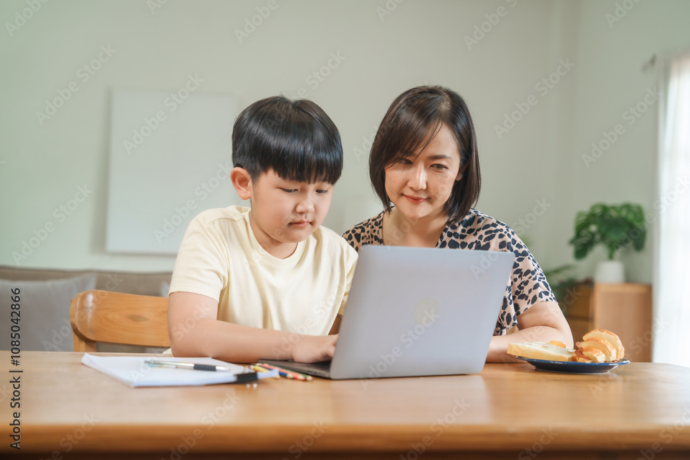 A mother teaches her son to study online at home, using a digital tablet for learning. They sit together at a table with snacks, promoting homeschooling and family bonding. A mother teaches her son to study online at home, using a digital tablet for learning. They sit together at a table with snacks, promoting homeschooling and family bonding.