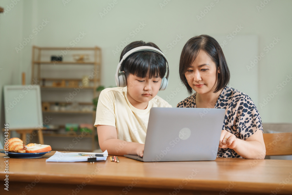A mother teaches her son to study online at home, using a digital tablet for learning. They sit together at a table with snacks, promoting homeschooling and family bonding. A mother teaches her son to study online at home, using a digital tablet for learning. They sit together at a table with snacks, promoting homeschooling and family bonding.
