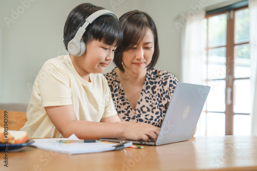 A mother teaches her son to study online at home, using a digital tablet for learning. They sit together at a table with snacks, promoting homeschooling and family bonding.