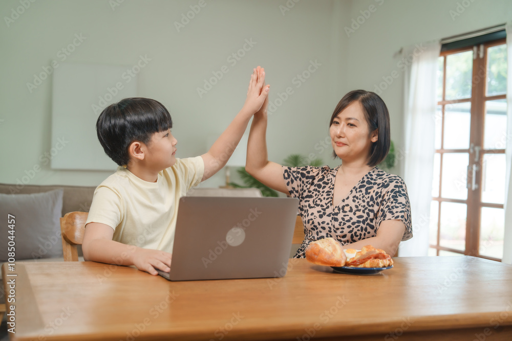 An Asian mother and son sit at the table and sofa, sharing time together while looking at a computer, tablet, and phone. They bond through technology and family activities An Asian mother and son sit at the table and sofa, sharing time together while looking at a computer, tablet, and phone. They bond through technology and family activities
