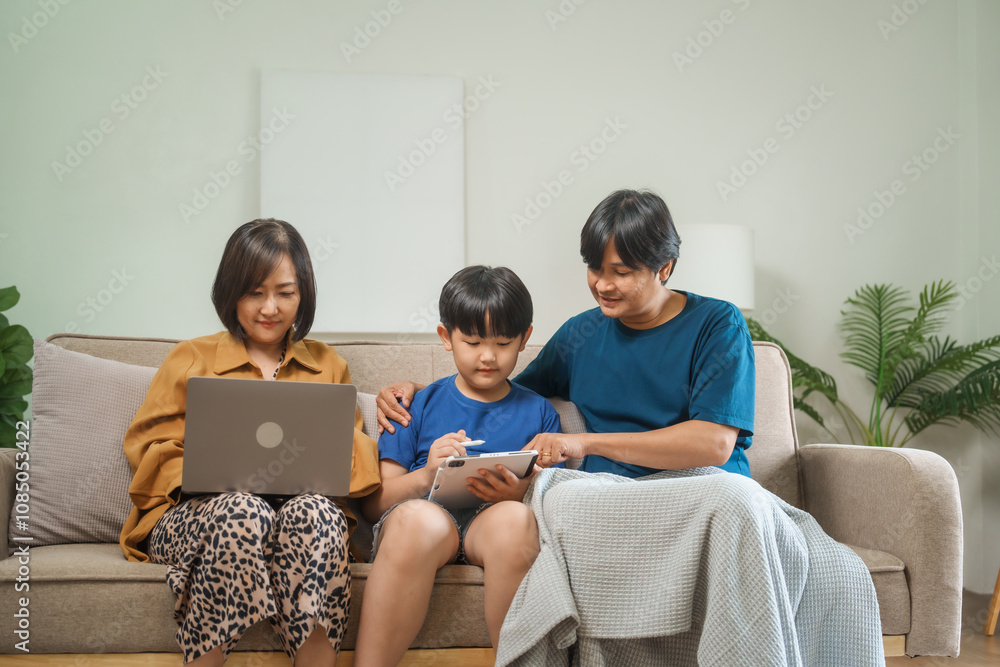 Asian parents and children sit together on a sofa at home, laughing and enjoying family time while using various devices like laptops, phones, and tablets, showcasing a tech-savvy lifestyle Asian parents and children sit together on a sofa at home, laughing and enjoying family time while using various devices like laptops, phones, and tablets, showcasing a tech-savvy lifestyle