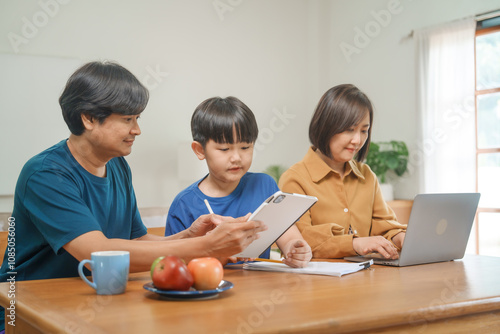 Asian parents and their children sit together at the table in the morning, studying online using tablets and computers, fostering a productive and focused family learning environment photo