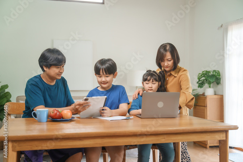 Wallpaper Mural Asian parents and their children sit together at the table in the morning, studying online using tablets and computers, fostering a productive and focused family learning environment Torontodigital.ca