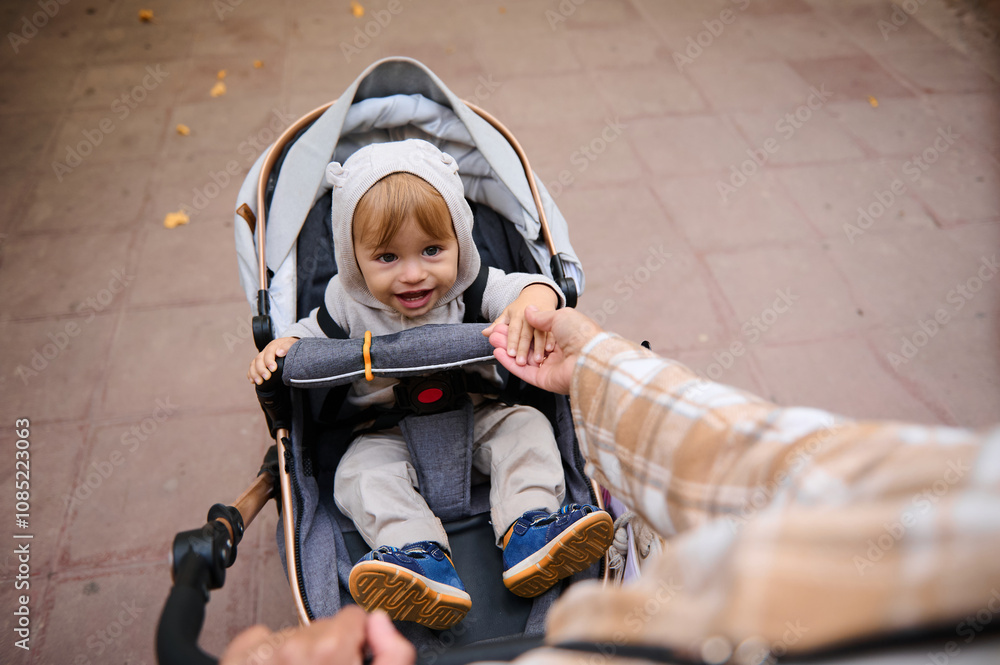 Smiling toddler in stroller holding parent's hand during a walk Smiling toddler in stroller holding parent's hand during a walk