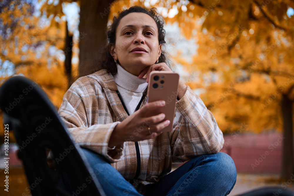 Woman in autumn park using smartphone with thoughtful expression Woman in autumn park using smartphone with thoughtful expression
